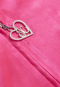 Giacca fucsia con zip realizzata in materiale morbido, dotata di un ciondolo a forma di cuore argentato con dettagli in strass.