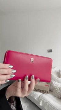 Roze leren portemonnee met gouden hardware, voorzien van een logo. Ritssluiting, gladde textuur en rechthoekige vorm. Patroonloos ontwerp.