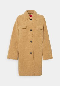 Cappotto teddy morbido color beige con colletto, chiusura frontale a bottoni, due tasche sul petto e maniche lunghe. Tessuto texture e silhouette oversize.