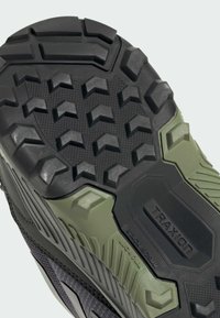 Gummisula med ett robust mönster och uttalade klackar, strukturerad yta och en blandning av svart och olivgrönt.