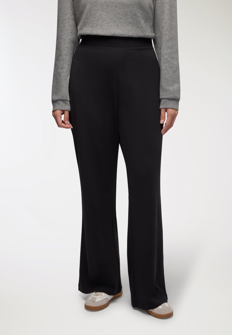 Pantaloni neri a gamba larga realizzati in un materiale morbido ed elastico, con una vita alta e elastica. Abbinati a un top grigio a maniche lunghe e calzature casual.