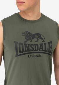 Olivovo zelené tielko bez rukávov vyrobené z bavlny, s výrazným čiernym logom leva a textom "Lonsdale London" v tučnom písme.