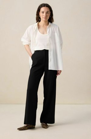 White oversized shirt, cream tank top, black wide-leg pants, and brown snake print flats. Smooth fabric, relaxed fit, simple design.