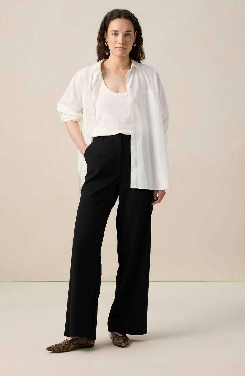 Chemise oversize blanche, débardeur crème, pantalon large noir et ballerines imprimé serpent marron. Tissu lisse, coupe décontractée, design simple.