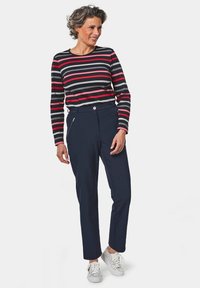 Gestreepte langarmshirt in zwart, rood en grijs, gecombineerd met marineblauwe broeken met voorzakken met rits en witte sneakers.