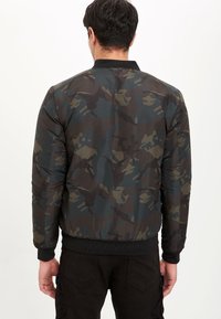 Giacca bomber con motivo mimetico scuro, realizzata in tessuto liscio, con polsini e orlo a coste e un design semplice del colletto.