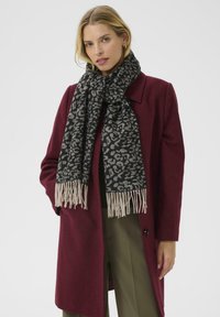 Black and gray leopard print scarf with fringed ends, made from soft material; worn over a burgundy coat, featuring a tailored design.