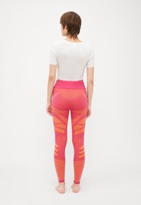 Pink leggings with a wide waistband, featuring geometric patterns in bright orange and textured sections. Smooth material, form-fitting design.