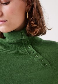 Maglione a collo alto verde in maglia con texture a coste, dotato di una patta con bottoni sulla spalla sinistra e un design aderente.