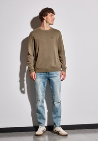 Kaki stickad tröja med rund halsringning, med långa ärmar. Kombinerad med ljusblå denimjeans och beige sneakers.