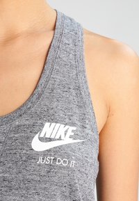 Šedý tank top Nike s kulatým výstřihem, ribovanou texturou a výrazným bílým logem s textem "JUST DO IT".
