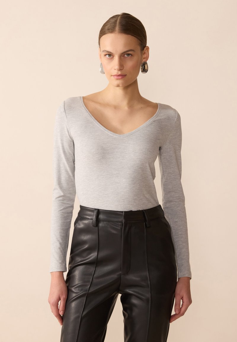 Top gris de manga larga y escote en V, hecho de una tela suave, combinado con pantalones de cuero negro de talle alto, que presentan costuras estructuradas y un ajuste entallado.