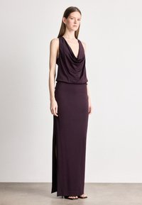 Φόρεμα χωρίς μανίκια σε σκούρο μωβ ύφασμα, με σχέδιο που αγκαλιάζει το σώμα και πλαϊνές σκισίματα για ευκολία κινήσεων. Λείο υφή.