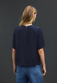 Marinebluse med et tekstureret bladmønster, korte ærmer og detaljer med nøglehul i ryggen. Matchet med lyseblå, højtaljede jeans.