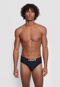 Schwarze Baumwollunterhose mit einem weißen Levi's-Logo am Bund, in klassischem Schnitt und glatter Textur. Das Modell steht aufrecht, keine Kleidung darüber.