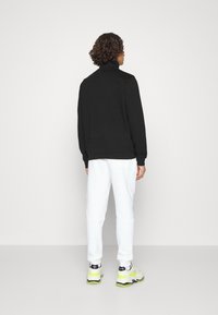 Zwarte sweatshirt met hoge kraag, ontspannen pasvorm, gecombineerd met witte sweatpants. Bevat elastische manchetten en enkels, gedragen met chunky sneakers.