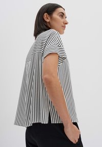 Blusa a maniche corte a righe bianche e nere, con vestibilità comoda, orlo arrotondato e spacchi laterali, realizzata in tessuto leggero.