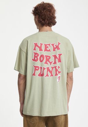 Jasnozielona, luźna koszulka wykonana z bawełny, z wyraźnym czerwonym napisem z tyłu, który brzmi "NOWO NARODZONY PUNK". Prosty design, z krótkimi rękawami.