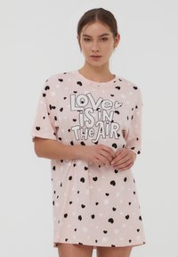 Gonna notte rosa a maniche corte con un motivo a cuori in bianco e nero. Presenta il testo "L'amore è nell'aria" in grassetto nero.