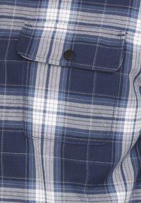 Marine-rutigt skjorta med horisontella och vertikala ränder i vitt och ljusblått. Inkluderar en bröstficka med en svart tryckknapp.