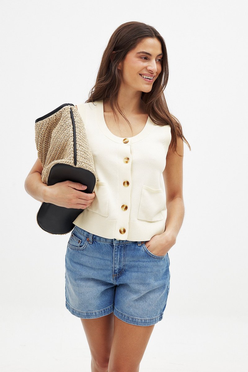 Krēmveida ribota tank topa ar zelta pogām un divām priekšējām kabatām; pārī ar zilu džinsu īsu bikses. Tur rokās teksturēta brūna un melna soma.