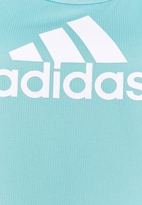 Jasnoniebieska koszulka sportowa z prążkowanego materiału, z dużym białym logo Adidas i trzema ukośnymi paskami w lewym górnym rogu.