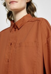 Camisa rustica de botão, feita de tecido leve, com colarinho, um bolso no peito e textura suave com detalhes de costura mínimos.