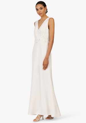 Robe de soirée blanche avec un décolleté en V profond, un corsage froncé et une broderie florale à la taille. Tissu fluide avec un léger brillant.