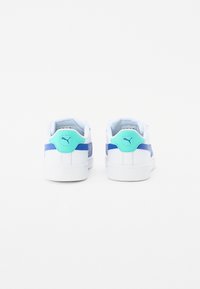 Baskets blanches avec des accents bleus, présentant une texture lisse, un col rembourré et une languette arrière turquoise. Design minimaliste et forme basse.
