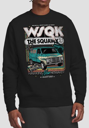 Person wearing black sweatshirt with vintage-style graphic of a turquoise van, tape cassette, radio, and the text "WSQK The Squawk 94.5 FM."