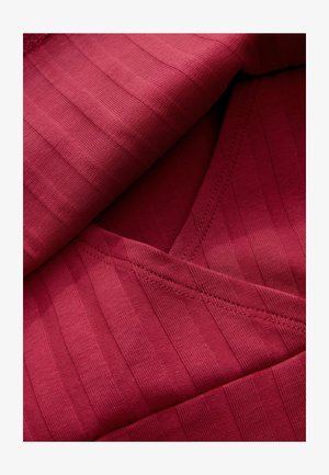 Červená rebrovaná tkanina s jemnou textúrou, zdobená výstrihom do V a detailom prekladu, zvýraznená jemnými švami.