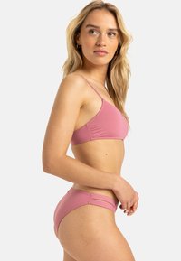 Różowy zestaw bikini z wąskimi ramiączkami i klasycznym krojem. Miękki materiał z gładką teksturą i minimalistycznym wzornictwem. Dwa ramiączka na plecach.