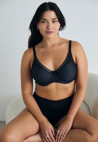 Schwarzer BH mit Netzdetails und verstellbaren Trägern, der ein geometrisches Muster aufweist und von einem passenden hochgeschnittenen Slip ergänzt wird.