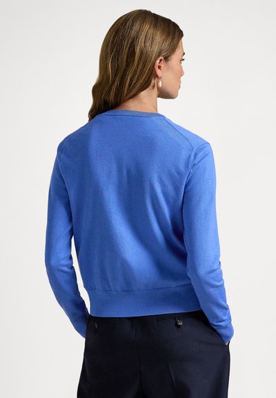 Μπλε πουλόβερ με μακριά μανίκια, στρογγυλή λαιμόκοψη και ριμπ τελείωμα. Κατασκευασμένο από απαλό ύφασμα με λεία υφή. Η φωτογραφία δείχνει τη λεπτομέρεια στην πλάτη.