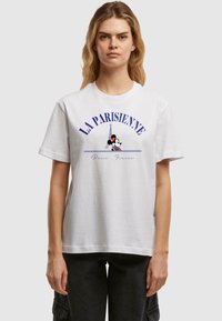 White cotton t-shirt featuring blue "LA PARISIENNE" text with an Eiffel Tower graphic and a small Mickey Mouse illustration at the center.