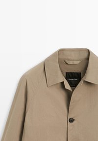 Giacca beige con bottoni, collo a punta e etichetta nera interna con il marchio "Massimo Dutti".