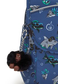 Sac à dos bleu marine avec des motifs aquatiques, présentant des requins et des poissons. Un porte-clés en forme de singe noir en fourrure attaché à un clip en métal.