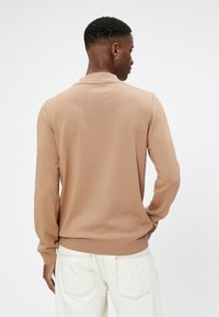 Suéter de punto beige con mangas largas y cuello con solapa, que presenta puños y dobladillo acanalados, mostrado desde la parte posterior.