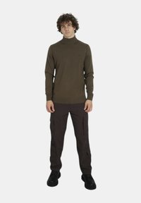 Maglione a collo alto marrone con orlo a coste, abbinato a pantaloni cargo marroni scuri con tasche con zip, completato da stivali neri.