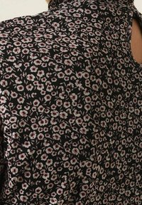 Tessuto nero a fantasia floreale con piccoli fiori rosa e bianchi, texture liscia, design aderente con un'apertura sullo scollo.
