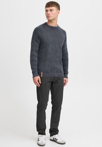 Pull en laine marine avec un motif texturé, col rond et poignets côtelés, associé à un pantalon sombre et des baskets blanches avec des rayures noires.