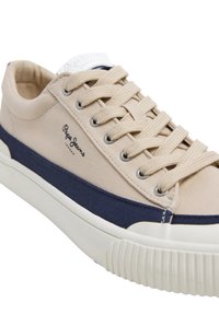 Sneaker beige in tela con striscia in tessuto blu navy, punta rotonda, suola in gomma e occhielli metallici. Presenta lacci beige e logo di lato.