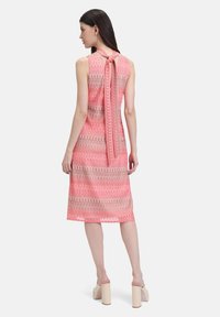 Ärmelloses Kleid in Pink und Beige mit einem gemusterten Design und einer Schleifendetail im Rücken. Der Saum fällt unter das Knie. Das Material wirkt strukturiert und hat ein leichtes Design.