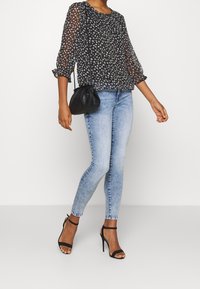 Czarna bluzka w kwiaty z przezroczystymi rękawami, zestawiona z jasnoniebieskimi skinny jeansami i czarnymi szpilkami. Stylizacja uzupełniona jest małą czarną torebką.