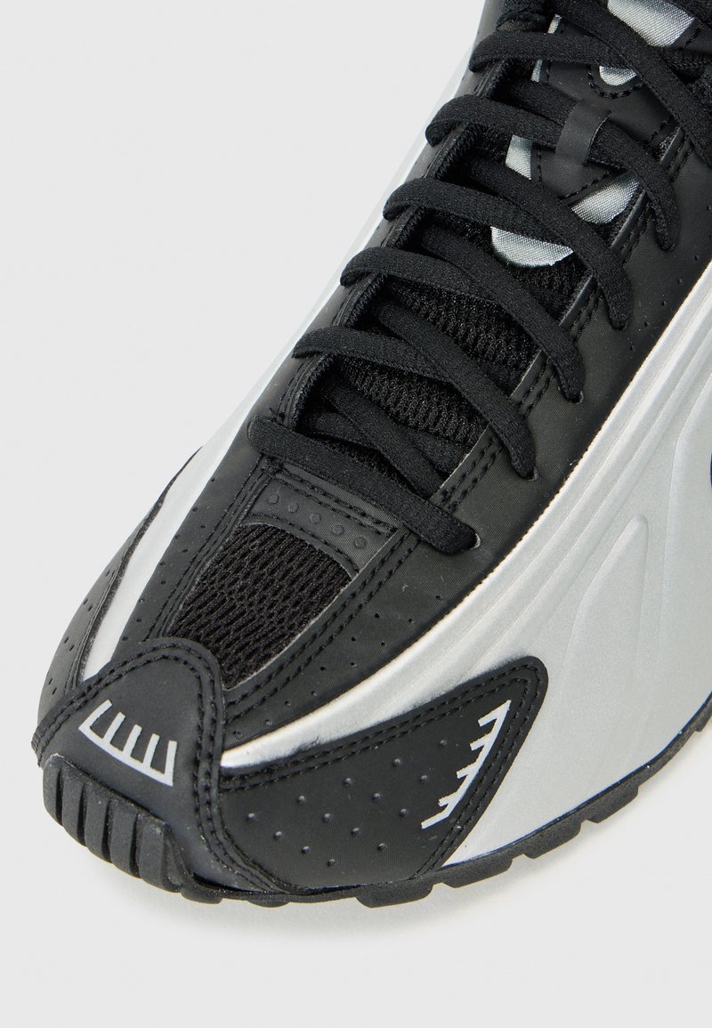 Baskets de sport noires avec un dessus en maille, des accents argentés, un embout texturé et une semelle en caoutchouc avec un motif de bande.