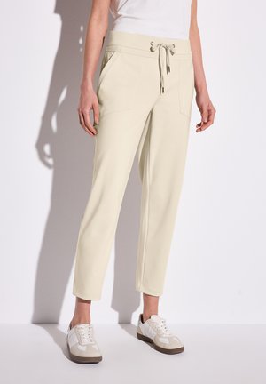 Light beige sweatpants with a wide elastic waistband and drawstring detail. Features angled front pockets and tapered ankles.