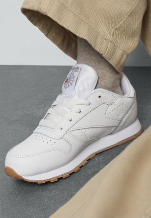 Zapatillas blancas de cuero con un acabado texturizado, detalles perforados y suela de goma. Cuenta con una lengüeta acolchada y un acento de logo.