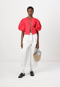 Top cropped rosso con maniche a palloncino e dettagli in argento, abbinato a pantaloni bianchi a gamba larga e una borsa intrecciata. Mocassini neri completano l'outfit.