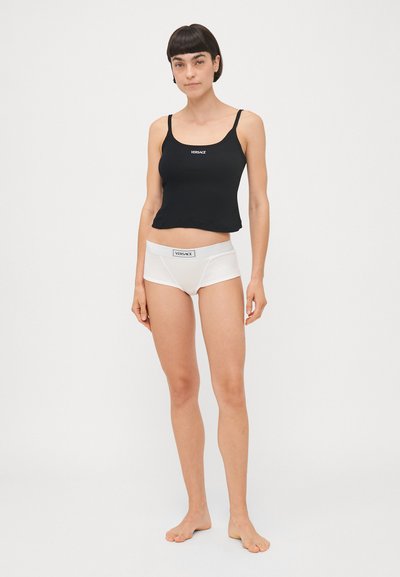 Zwarte cropped tanktop met dunne bandjes en een wit logo. Gecombineerd met witte boxershorts met een elastische tailleband en logo-accent.