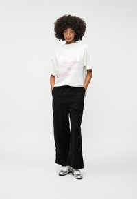 Valge graafiline T-särk roosa teksti ja mustritega, koos mustade laiade pükstega ja hõbedaste kingadega. Sile kangas ja lõdva istuvusega.